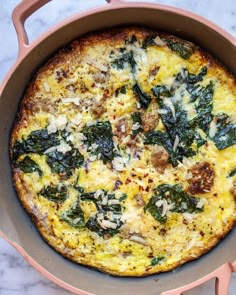 an omelet with spinach and cheese in a pink pan on a marble counter