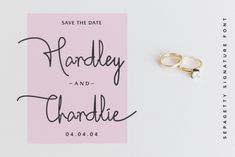 two gold wedding rings sitting on top of a pink save the date card next to each other