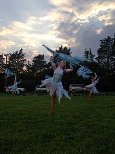 a group of young women dancing on top of a lush green field under a cloudy sky