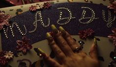 a woman's hands with yellow nail polish on top of a purple and silver sign