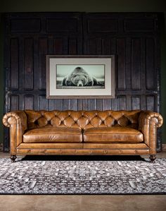 a brown leather couch sitting in front of a wooden wall with a painting on it