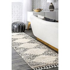 a white couch sitting on top of a wooden floor next to a rug covered in black and white pillows