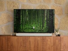 a flat screen tv sitting on top of a wooden cabinet in front of a stone wall