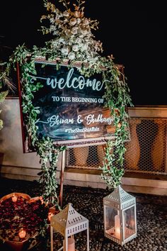 the welcome sign is decorated with greenery and lit candles for an outdoor wedding ceremony