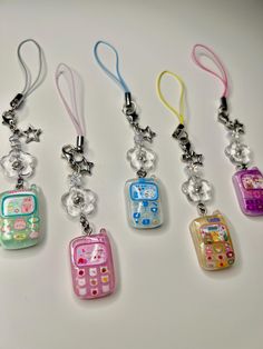 four different cell phones are hanging from lanyards on a white surface, one is pink, the other is blue