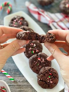 chocolate cookies with sprinkles and candy canes are being held by two hands