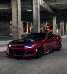 a red chevrolet camaro is parked in an empty parking garage with no one around