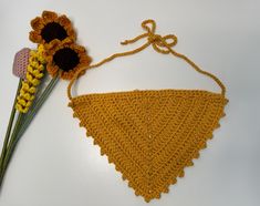 a crocheted triangle and two flowers on a white table with a string attached to it