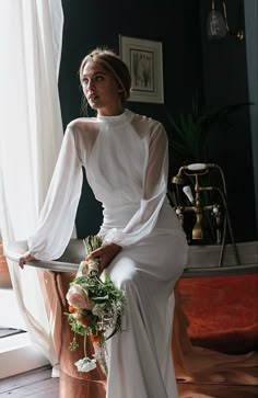 a woman in a white dress sitting on a chair with her hands on her hips