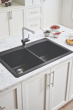 two black sinks in a white kitchen with marble counter tops