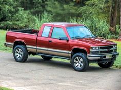 a red pick up truck parked on the side of a road in front of some trees