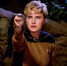 a woman in star trek uniform pointing at something with her hand and looking to the side