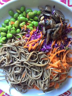 a white plate topped with noodles and veggies on top of a colorful table cloth