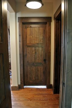 an empty hallway with a wooden door and light fixture on the ceiling above it, along with hardwood flooring