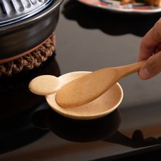 a person holding a wooden spoon on top of a black table next to other plates