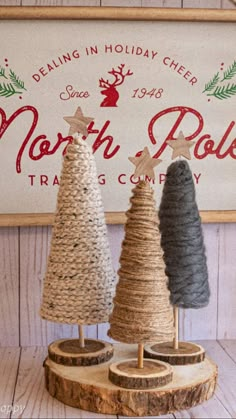 three small christmas trees sitting on top of a wooden stand in front of a sign