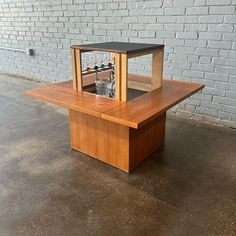 a wooden table with a black top on concrete floor next to brick wall and window