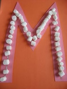 the letter m made out of marshmallows is displayed on an orange surface