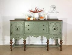 a green dresser with two vases on top of it and some pumpkins in the background