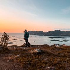 a woman standing on top of a grass covered hillside next to the ocean at sunset