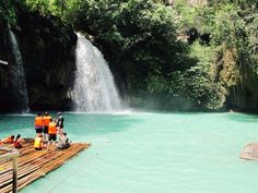 several people standing on rafts in front of a waterfall