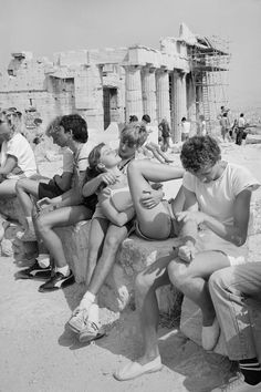 a group of people sitting next to each other on a stone bench in front of an old building