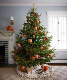 a decorated christmas tree with orange ornaments in a living room next to a fire place