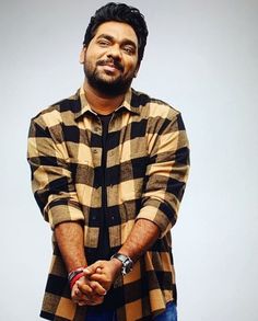 a man standing in front of a white background wearing a checkered shirt and jeans