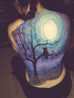 the back of a woman's body painted with an owl and tree at night