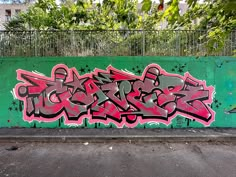 graffiti on the side of a green wall with trees in the backgrouund