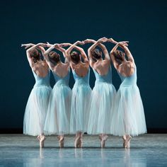 five ballerinas in blue tulle skirts and ballet shoes, with their arms stretched out