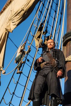 a man standing on top of a tall ship next to another man in black clothing