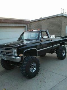 a large black truck parked in front of a garage with big tires on it's tires