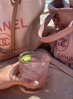 a person holding a drink in their hand on the beach with other purses behind them