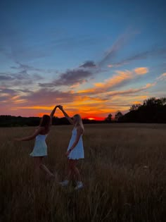 two girls are standing in a field with their hands together as the sun sets behind them