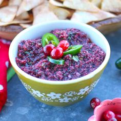 a bowl filled with cranberry sauce and garnished with green peppers next to chips