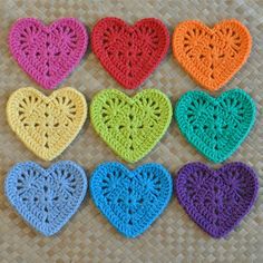 six crocheted hearts arranged in different colors on a woven tablecloth with wicker background