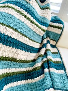 a blue and green crocheted blanket sitting on top of a white couch next to a window