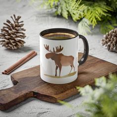 a moose mug sitting on top of a wooden board next to pine cones and cinnamon sticks