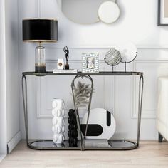 a console table with various items on it in front of a white wall and mirror