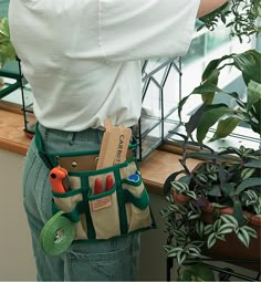 a person holding a tool belt in front of a potted plant with scissors and other tools