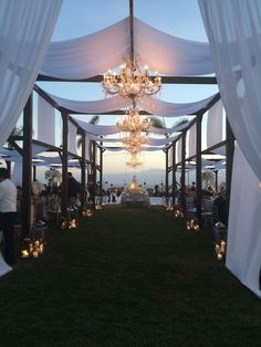 an outdoor wedding setup with chandeliers and white draping on the grass