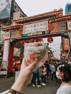 a person holding up a food item in front of a building with chinese writing on it