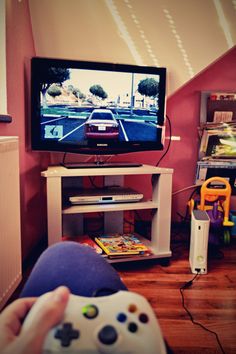 a person holding a video game controller in front of a flat screen tv with cars on it