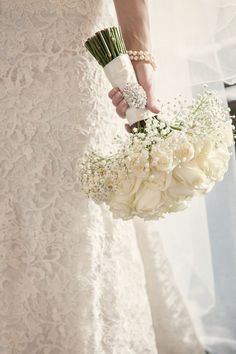 a woman in a wedding dress holding a bouquet of white roses and baby's breath