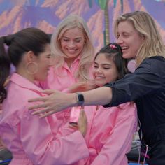 three women in pink robes are hugging each other while one woman holds her hand out