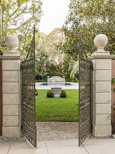 an open gate leading to a garden with a fountain