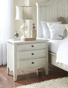 a white bed sitting next to a night stand with two lamps on top of it