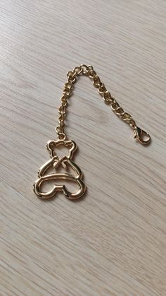 a gold chain with a teddy bear on it sitting on a wooden table next to a cell phone