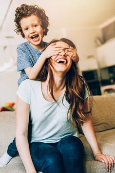 a woman sitting on top of a couch next to a little boy who is covering his eyes